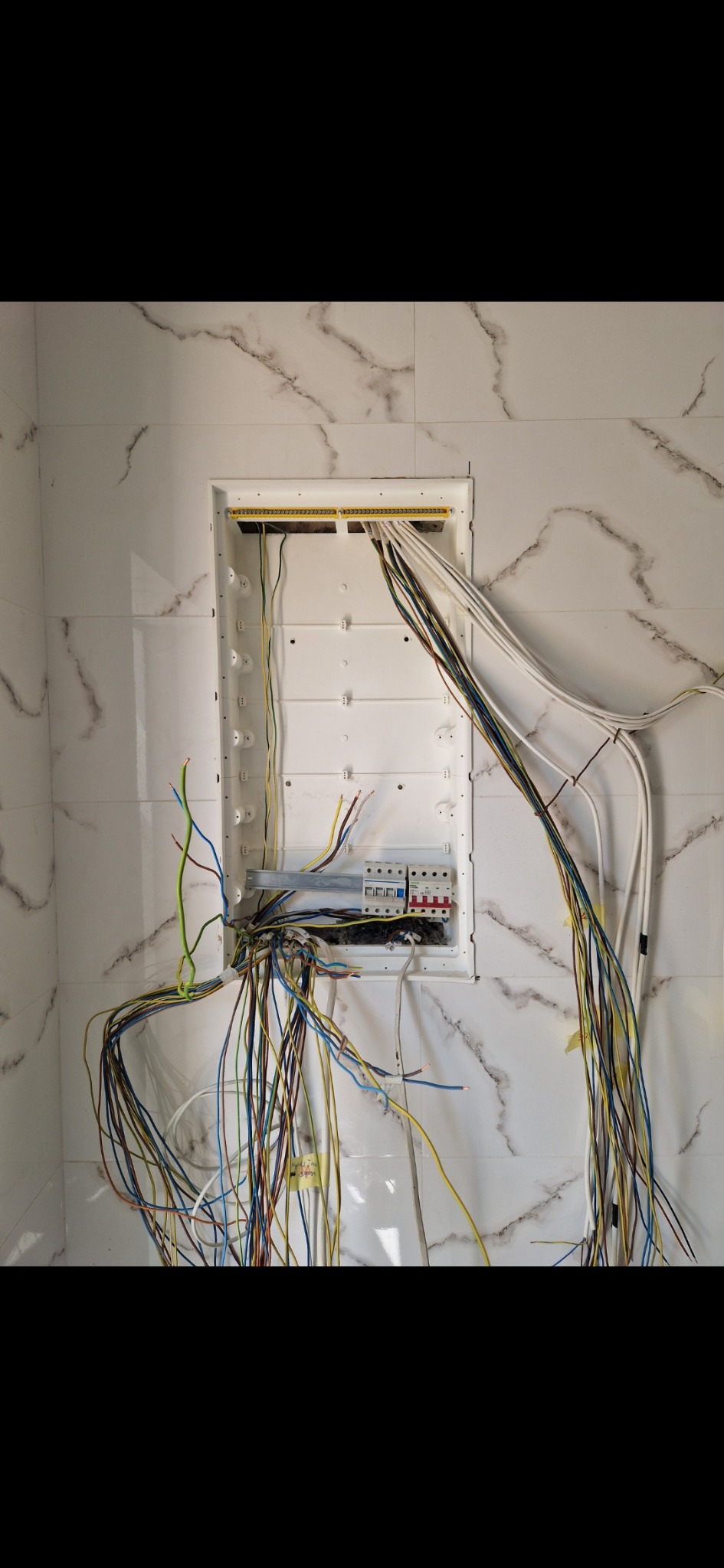 Rozdzielnia elektryczna w trakcie montażu, widoczne kable i zabezpieczenia na tle marmurowej ściany, Wrocław. Prace instalacyjne w nowym budynku.