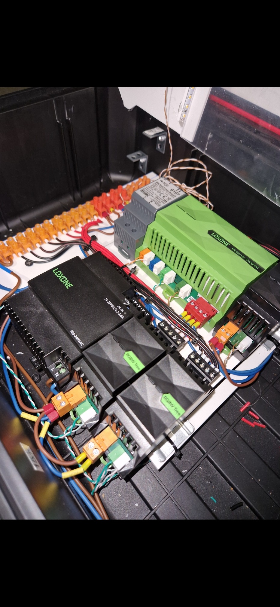 Rozdzielnica Loxone z modułami RGBW Tree i Miniserver Compact, zasilaczem oraz listwami zaciskowymi. Widoczne kable i przewody podłączone do urządzeń.