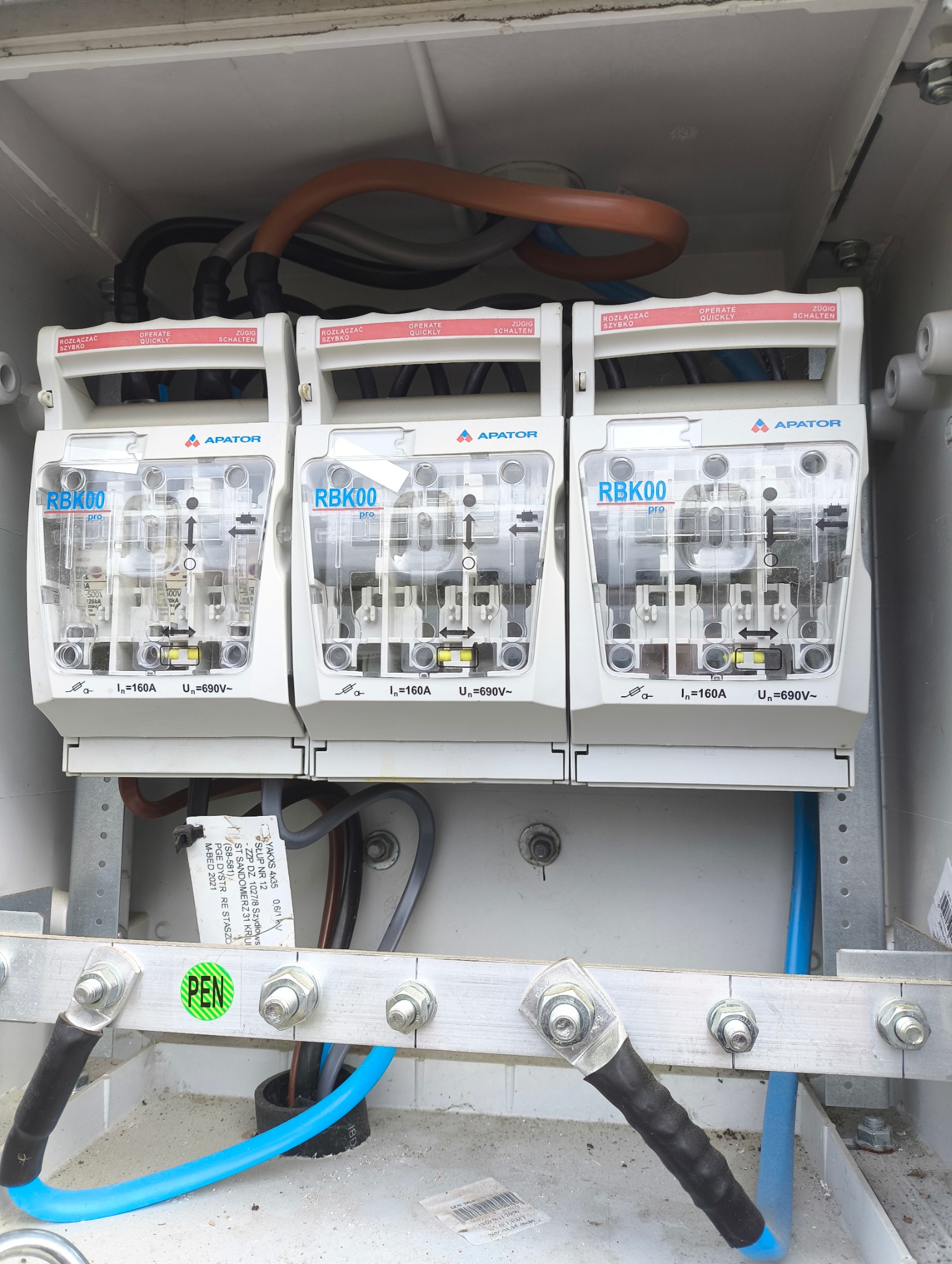Rozdzielnica elektryczna z trzema bezpiecznikami RBK00 firmy Apator, widoczne przewody i szyna PEN. Element instalacji elektrycznej w skrzynce.