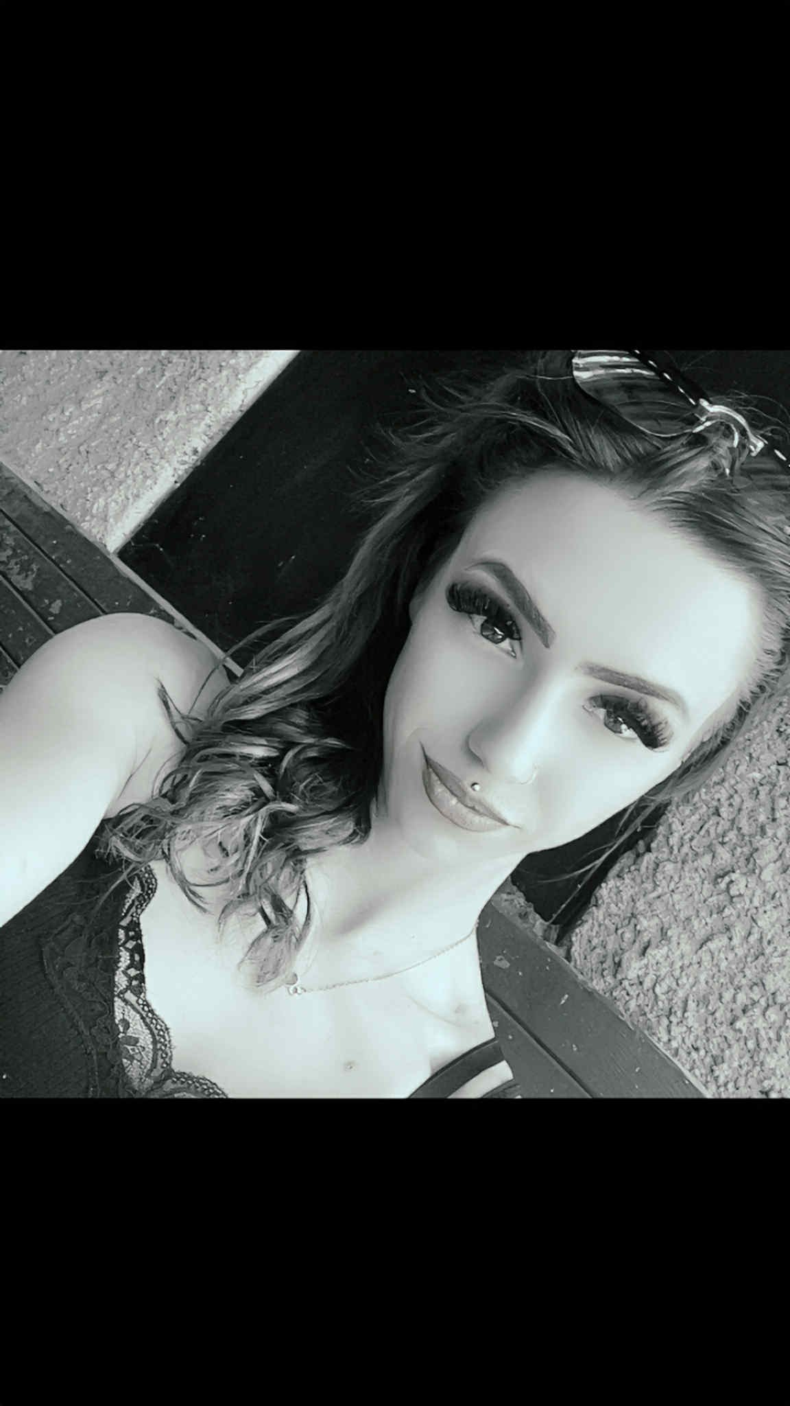 Portret kobiety z piercingiem w nosie i mocnym makijażem oczu, w czarno-białej tonacji, z włosami ułożonymi w fale i delikatnym naszyjnikiem.