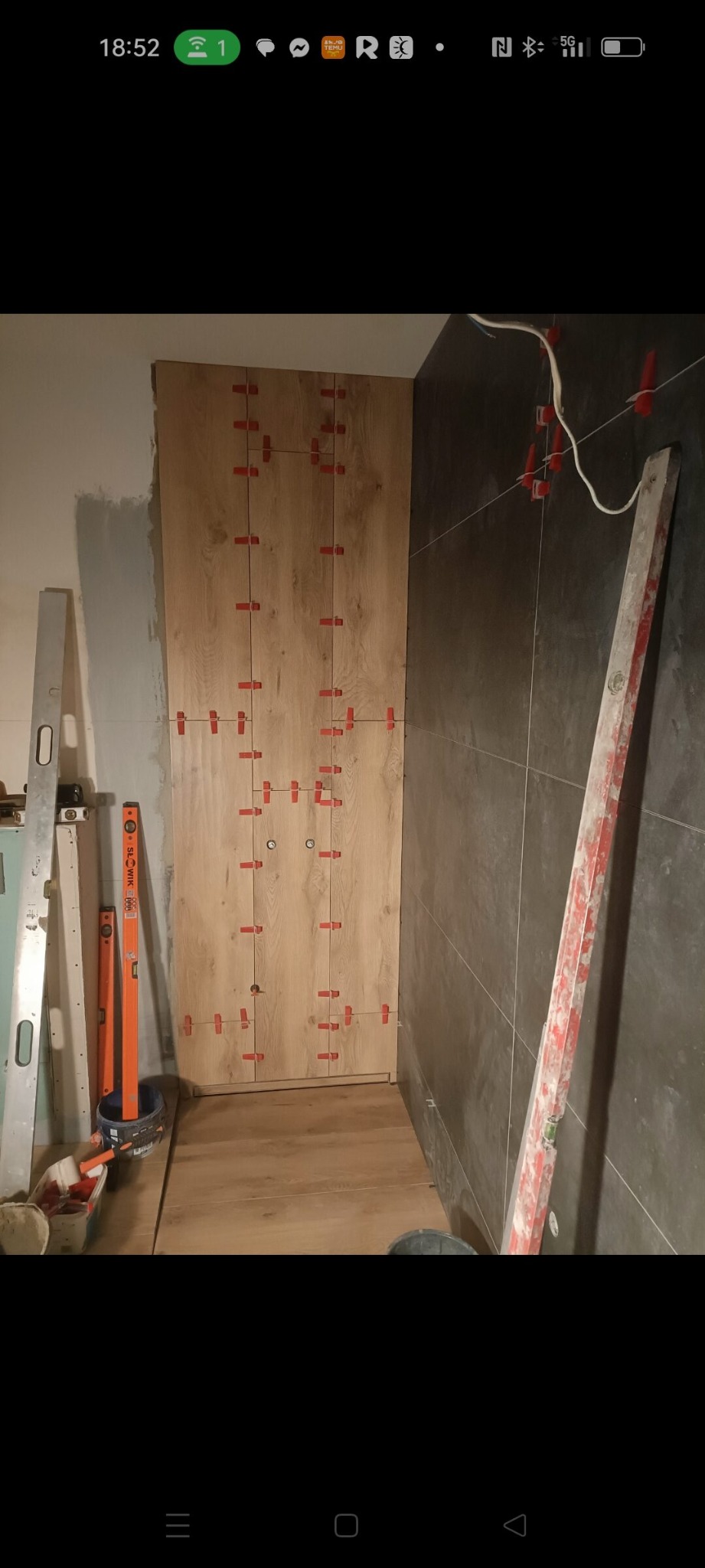 Układanie płytek imitujących drewno na ścianie w łazience, z użyciem czerwonych krzyżyków dystansowych. Widoczne poziomice i narzędzia glazurnicze.