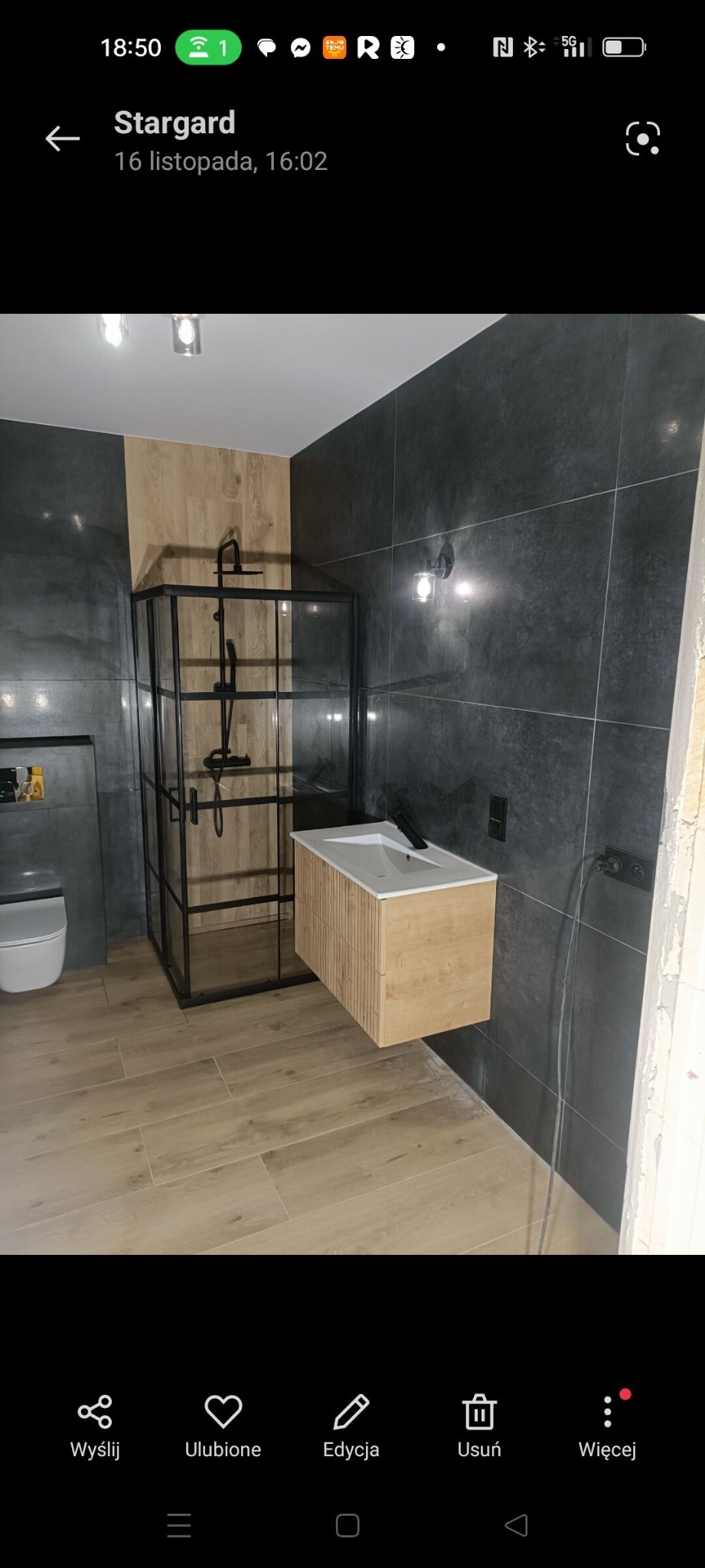 Nowoczesna łazienka po remoncie: kabina prysznicowa typu walk-in z czarnymi profilami, drewnopodobna szafka z umywalką, szare płytki na ścianach i podłodze.