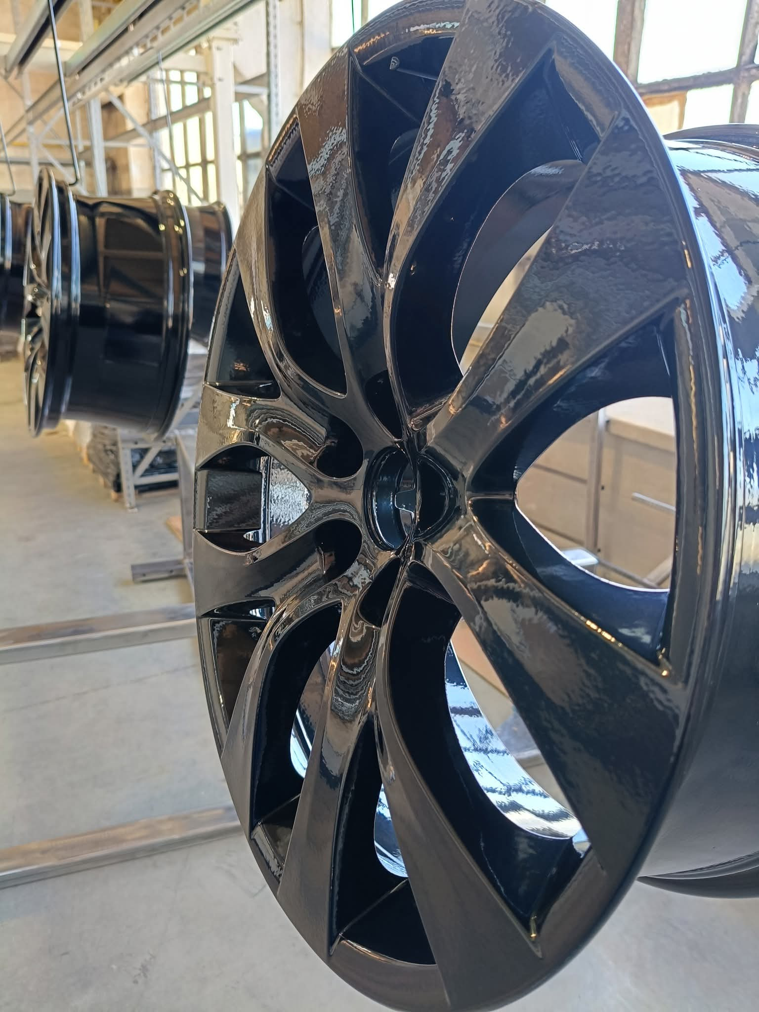 Błyszczące, czarne felgi aluminiowe zawieszone na metalowej konstrukcji, po procesie obróbki powierzchni. Widoczne refleksy światła.
