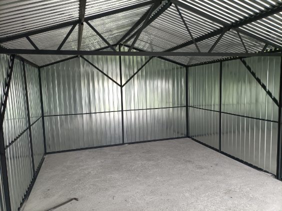 Wnętrze garażu blaszanego z widoczną konstrukcją stalową i ścianami z blachy falistej. Surowy beton na podłodze. Widok od wewnątrz, bez wyposażenia.