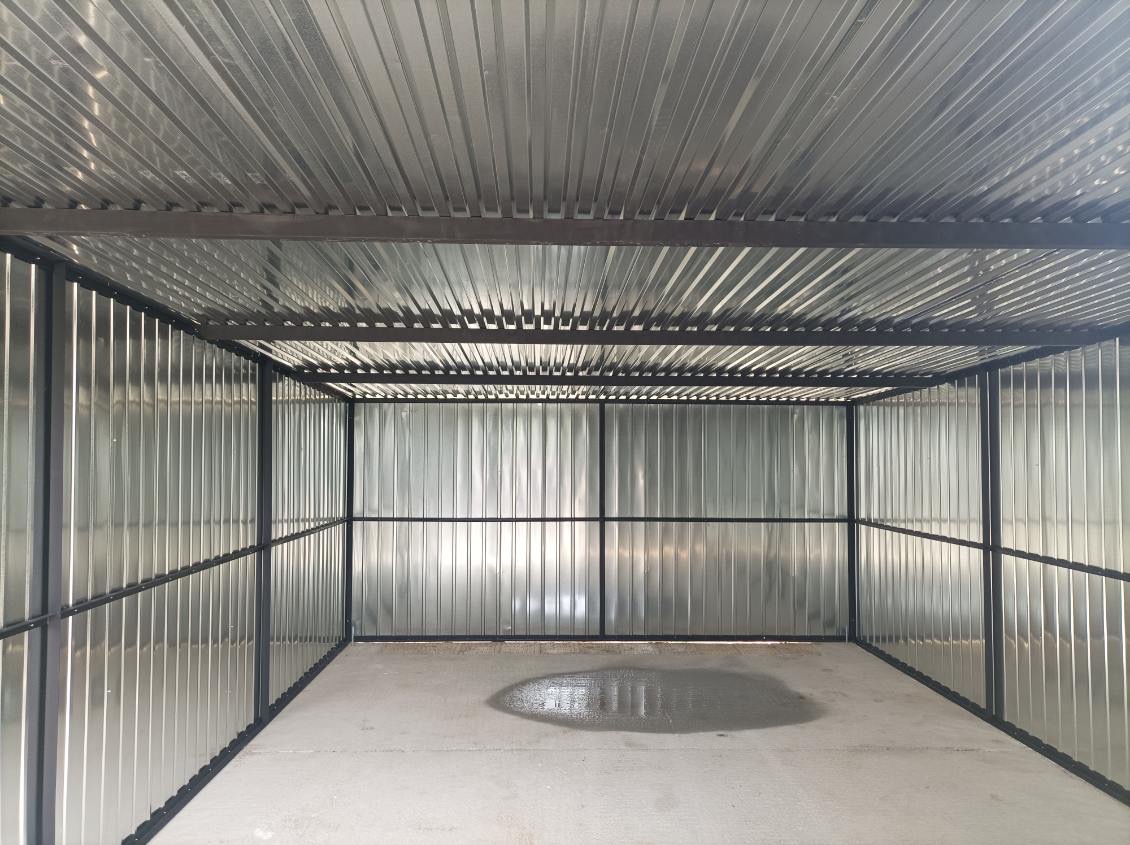 Wnętrze garażu blaszanego z metalową konstrukcją i podłogą betonową z plamą wody. Widok z dołu na sufit z blachy falistej.