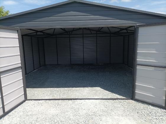 Otwarty, szary garaż blaszany z dwuskrzydłowymi drzwiami, widok na żwirowe podłoże i stalową konstrukcję dachu w słoneczny dzień.