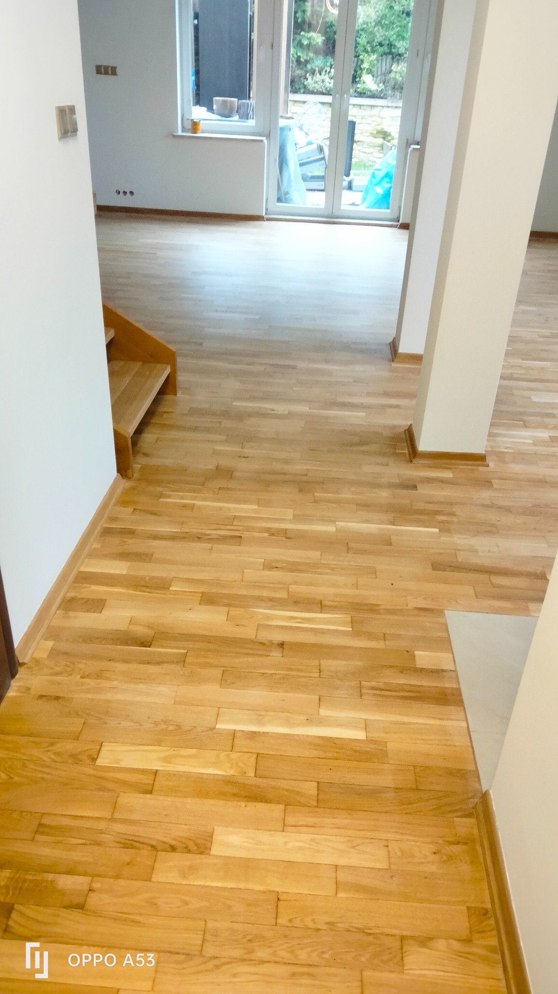 Ułożony parkiet w jasnym odcieniu drewna w przestronnym wnętrzu z oknami balkonowymi i schodami. Widok na świeżo wykończoną podłogę z bliska.