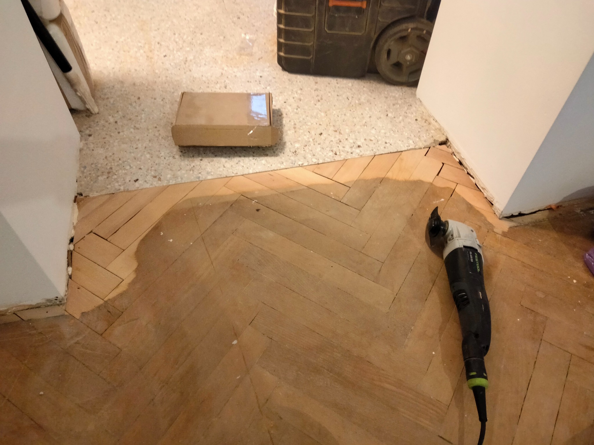 Ukończona część podłogi z parkietu w jodełkę, narzędzie do cięcia przy krawędzi. Prace parkieciarskie w Gdyni, widoczny fragment nowej podłogi.