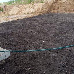 Zielony ogród - Przygotowany teren pod trawnik w Ornecie: wyrównana ziemia, widoczny brzeg chodnika i nasyp ziemny w tle. Gotowość do założenia trawy.