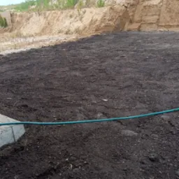 Przygotowany teren pod trawnik w Ornecie: wyrównana ziemia, widoczny brzeg chodnika i nasyp ziemny w tle. Gotowość do założenia trawy.