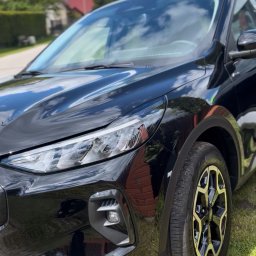 CarGlow Detailong - Lśniący, czarny SUV po myciu, z widocznym odbiciem nieba i chmur na karoserii. Detale felg i reflektorów podkreślone przez światło słoneczne. Auto stoi na trawie.