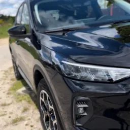 Błyszczący, czarny SUV na żwirowej drodze w słoneczny dzień. Widok z bliska na przedni reflektor i koło, z odbiciem chmur na karoserii.