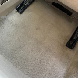 CarGlow Detailong - Jasna, wyczyszczona tapicerka podłogowa w samochodzie z widocznymi mocowaniami fotela. Delikatna faktura materiału i brak plam sugerują profesjonalne pranie.