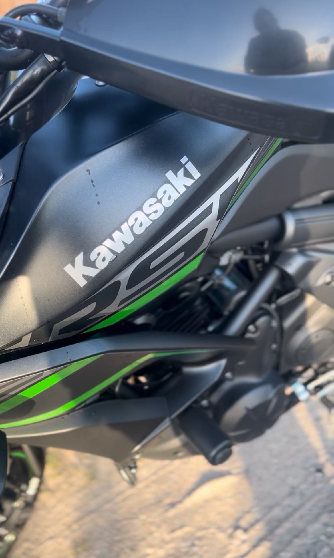 Fragment motocykla Kawasaki Z650 z zielonymi akcentami, widoczne logo i matowa, czarna karoseria. Ujęcie z bliska, podkreślające detale i nowoczesny design.