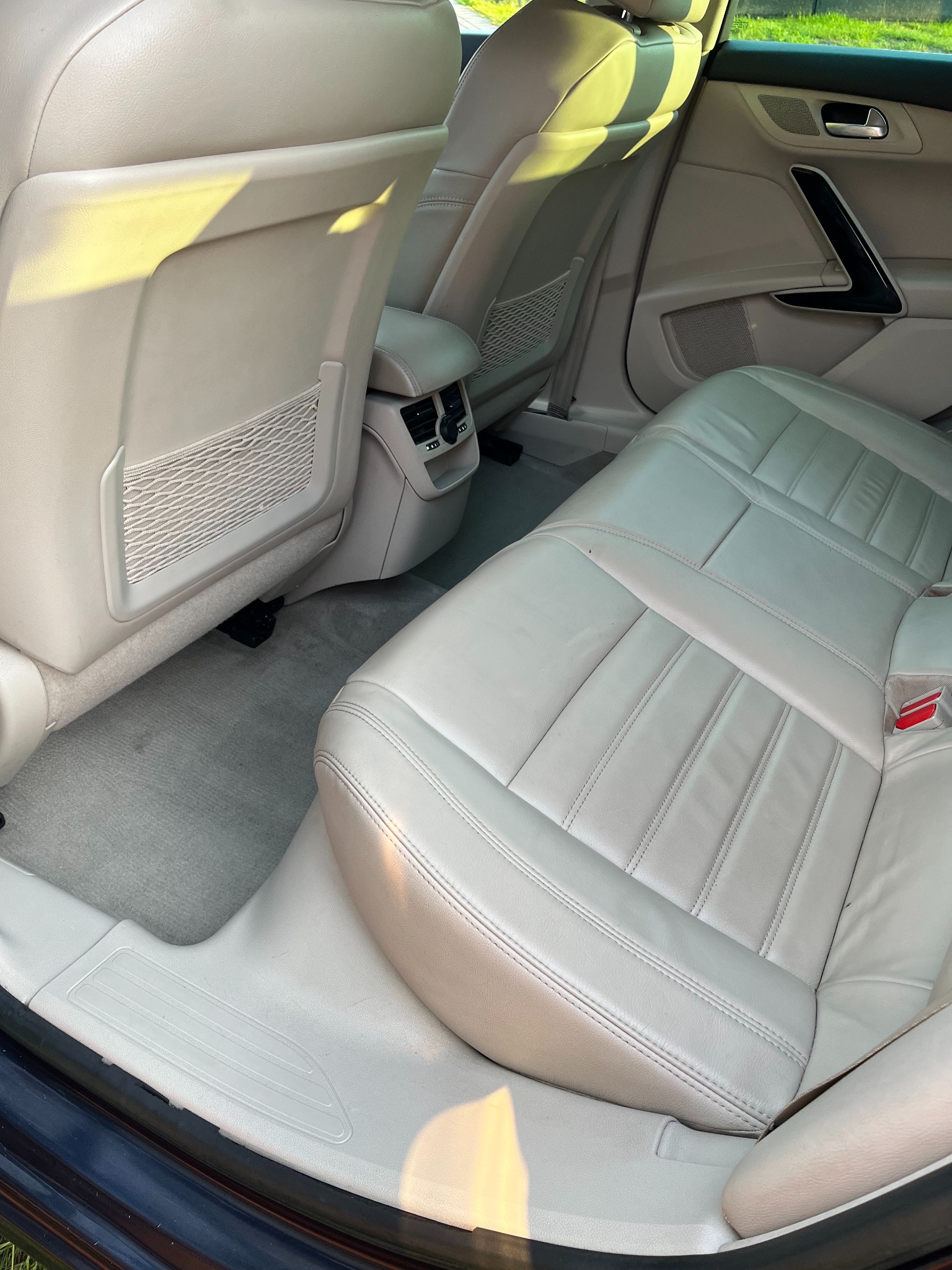 Jasne, skórzane tylne siedzenia w samochodzie, z widoczną siatką w kieszeni fotela i elementami wentylacji. Ujęcie wnętrza pojazdu w neutralnej tonacji.