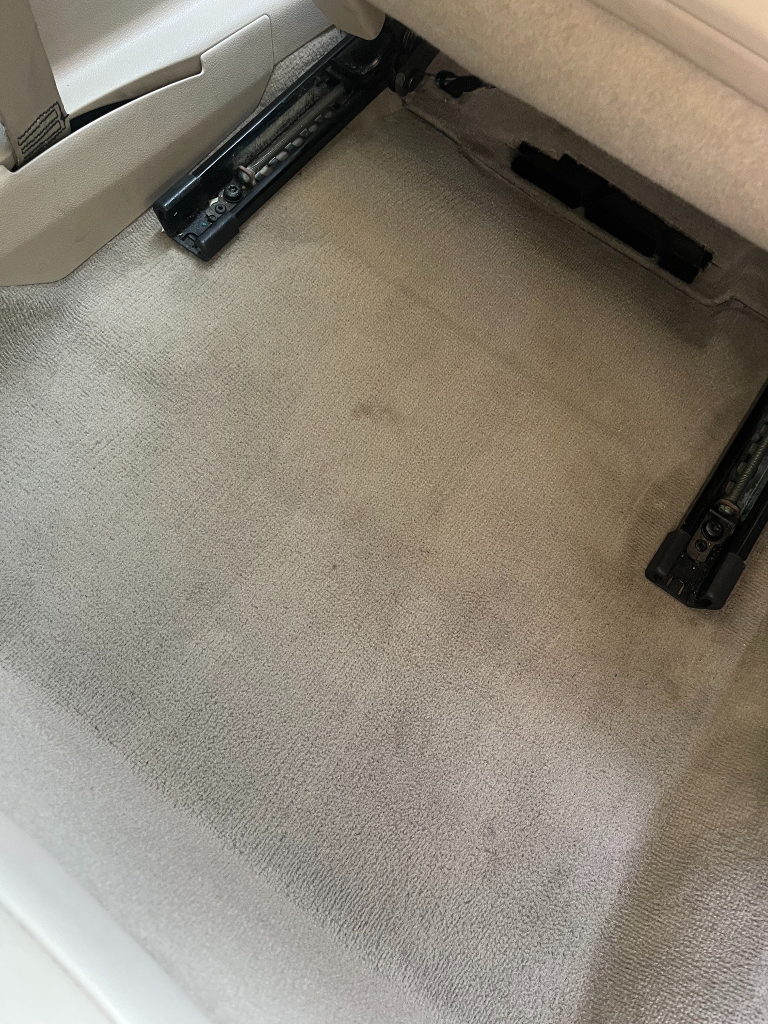 Jasna, wyczyszczona tapicerka podłogowa w samochodzie z widocznymi mocowaniami fotela. Delikatna faktura materiału i brak plam sugerują profesjonalne pranie.