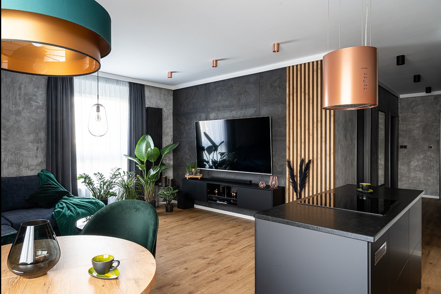 Nowoczesny salon z drewnianą podłogą, zielonymi akcentami i ścianą z dekoracyjnymi panelami. Centralnie umieszczony telewizor i designerski okap.