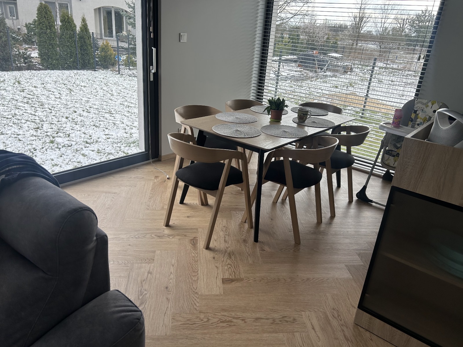 Jasna podłoga ułożona w jodełkę francuską, widoczna spod stołu z krzesłami w nowoczesnym wnętrzu z oknem na ogród pokryty śniegiem. skleppodlogi.pl