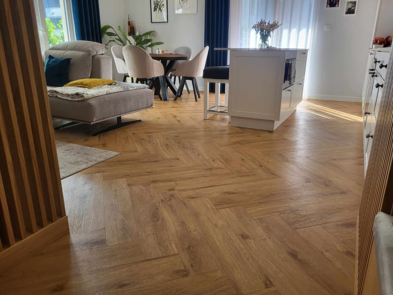 Salon z parkietem ułożonym we wzór jodełki francuskiej. Jasne drewno, nowoczesne meble, naturalne światło wpadające przez okno.