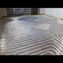KM Instal Michał Kozyra - Białe rury ogrzewania podłogowego ułożone na siatce, widoczne zielone znaczniki. Przygotowanie do wylewki.