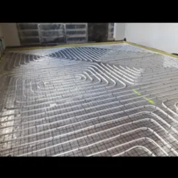 Białe rury ogrzewania podłogowego ułożone na siatce, widoczne zielone znaczniki. Przygotowanie do wylewki.