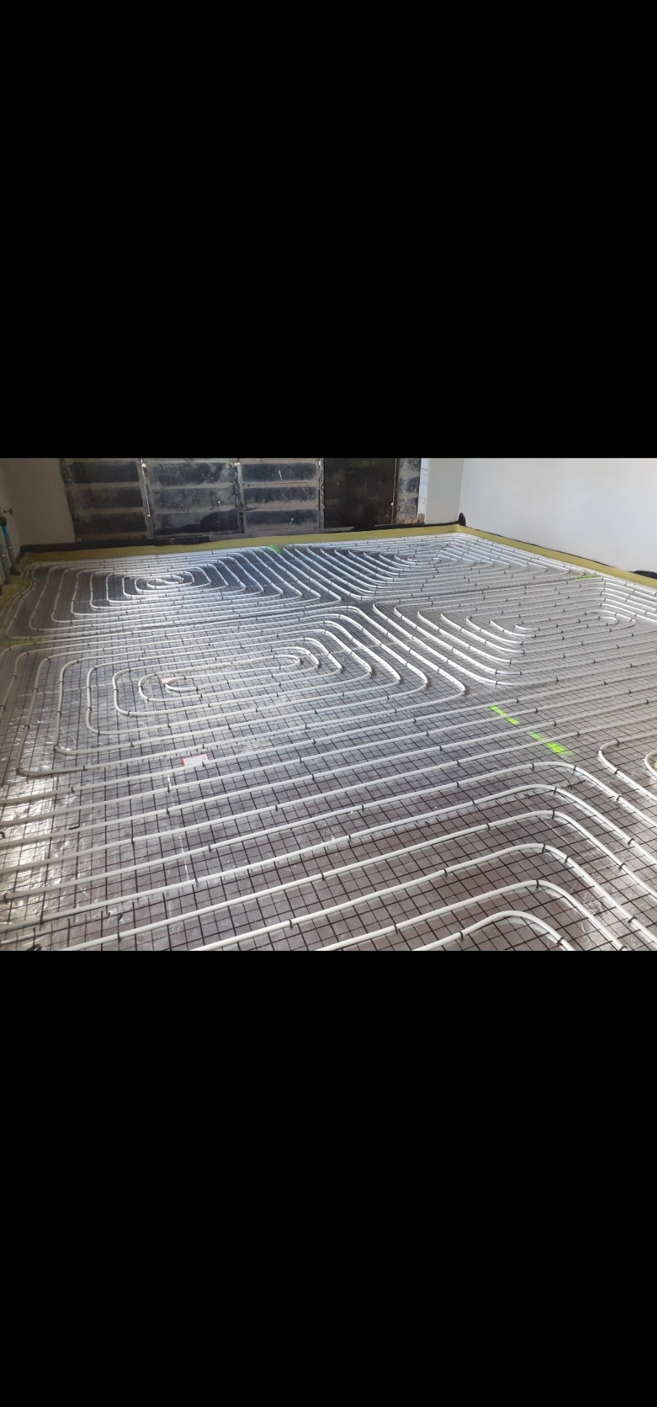 Białe rury ogrzewania podłogowego ułożone na siatce, widoczne zielone znaczniki. Przygotowanie do wylewki.
