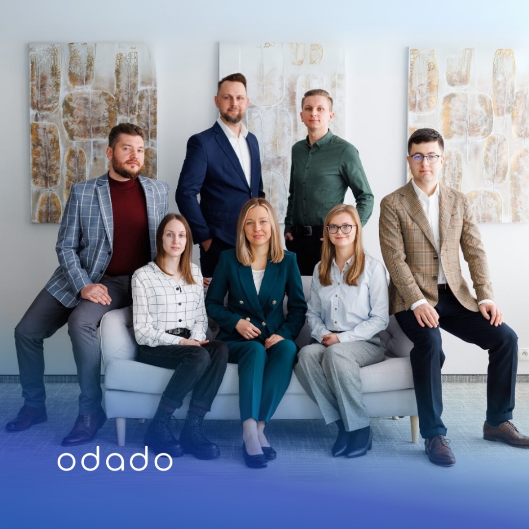 Zespół marketingowy Odado.pl w eleganckich strojach pozuje na kanapie, na tle nowoczesnych obrazów. Uśmiechnięci, w formalnych stylizacjach, gotowi do działania.