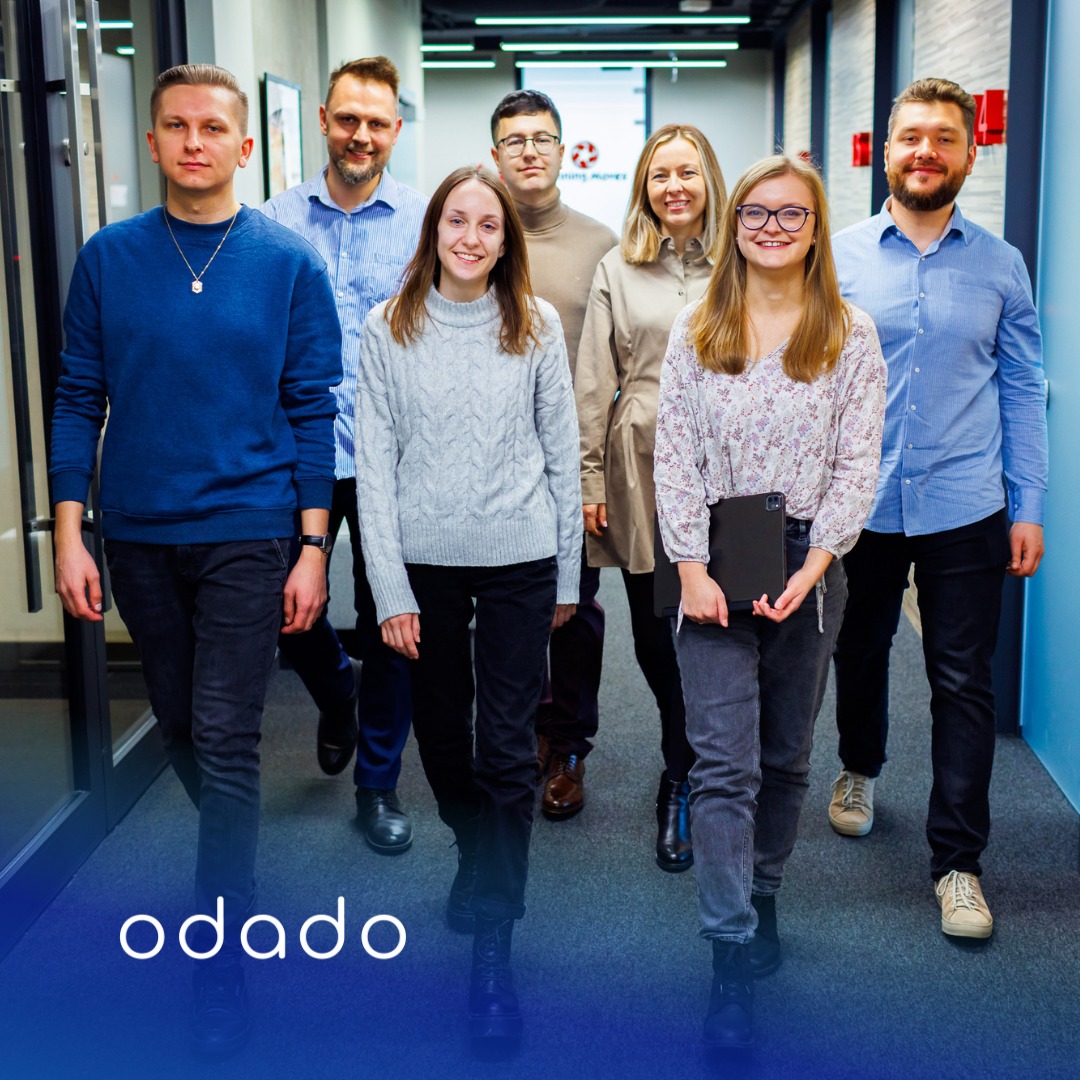 Zespół Odado w korytarzu biurowym, uśmiechnięci i idący w stronę kamery. Jasne oświetlenie podkreśla pozytywną atmosferę w firmie.