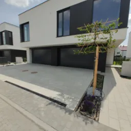 Nowoczesny dom z czarnymi bramami garażowymi i oknami, jasna kostka brukowa na podjeździe, ozdobne drzewko. Minimalistyczny design, słoneczny dzień.