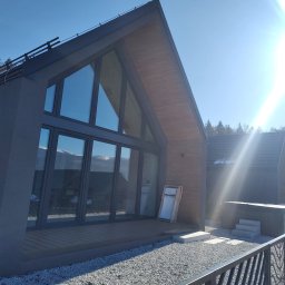 FINESTRA DAWID ZATOR - Nowoczesny dom z dużymi oknami aluminiowymi i przesuwnymi drzwiami tarasowymi, widok z zewnątrz na tle błękitnego nieba i gór. Minimalistyczna architektura.