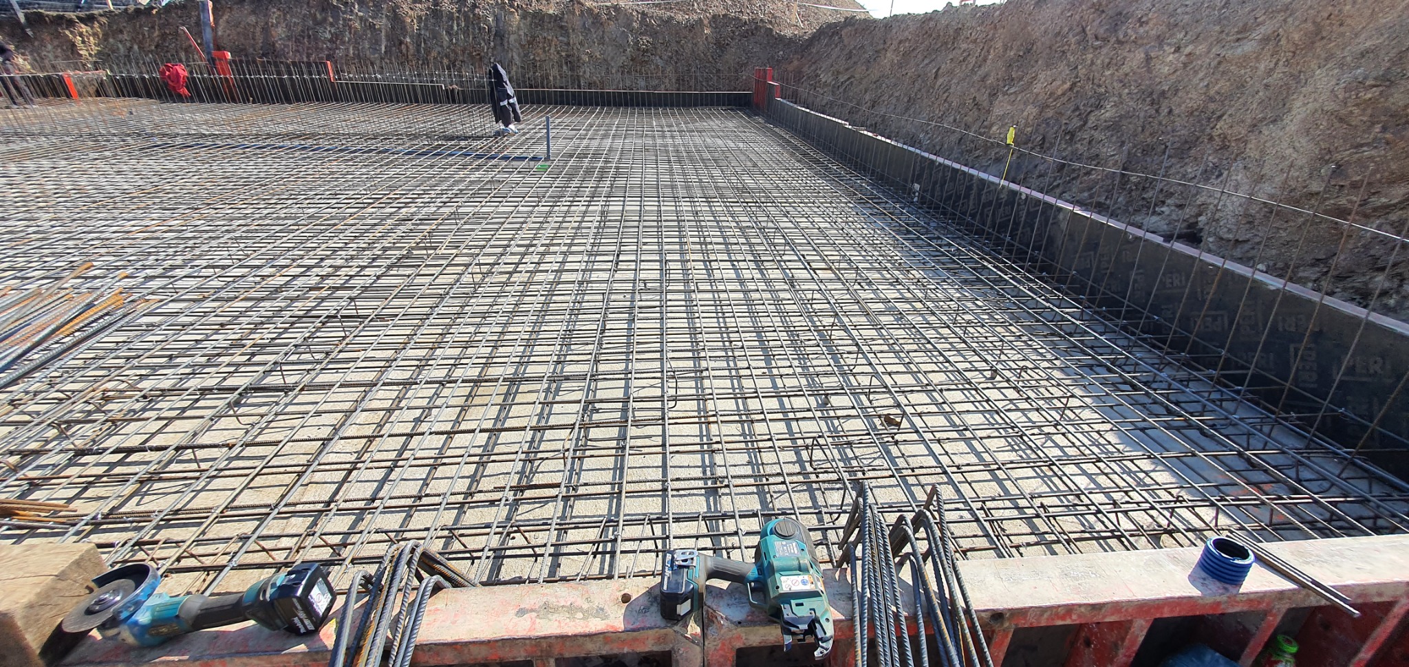 Siatka zbrojeniowa na przygotowanym podłożu, widoczne narzędzia zbrojarskie i szalunki, grunt w tle.
