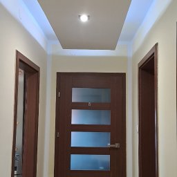 Firma uslugowa - Korytarz po remoncie: drewnopodobna podłoga, brązowe drzwi z przeszkleniami i podwieszany sufit z oświetleniem LED. Widok na dwie pary drzwi.