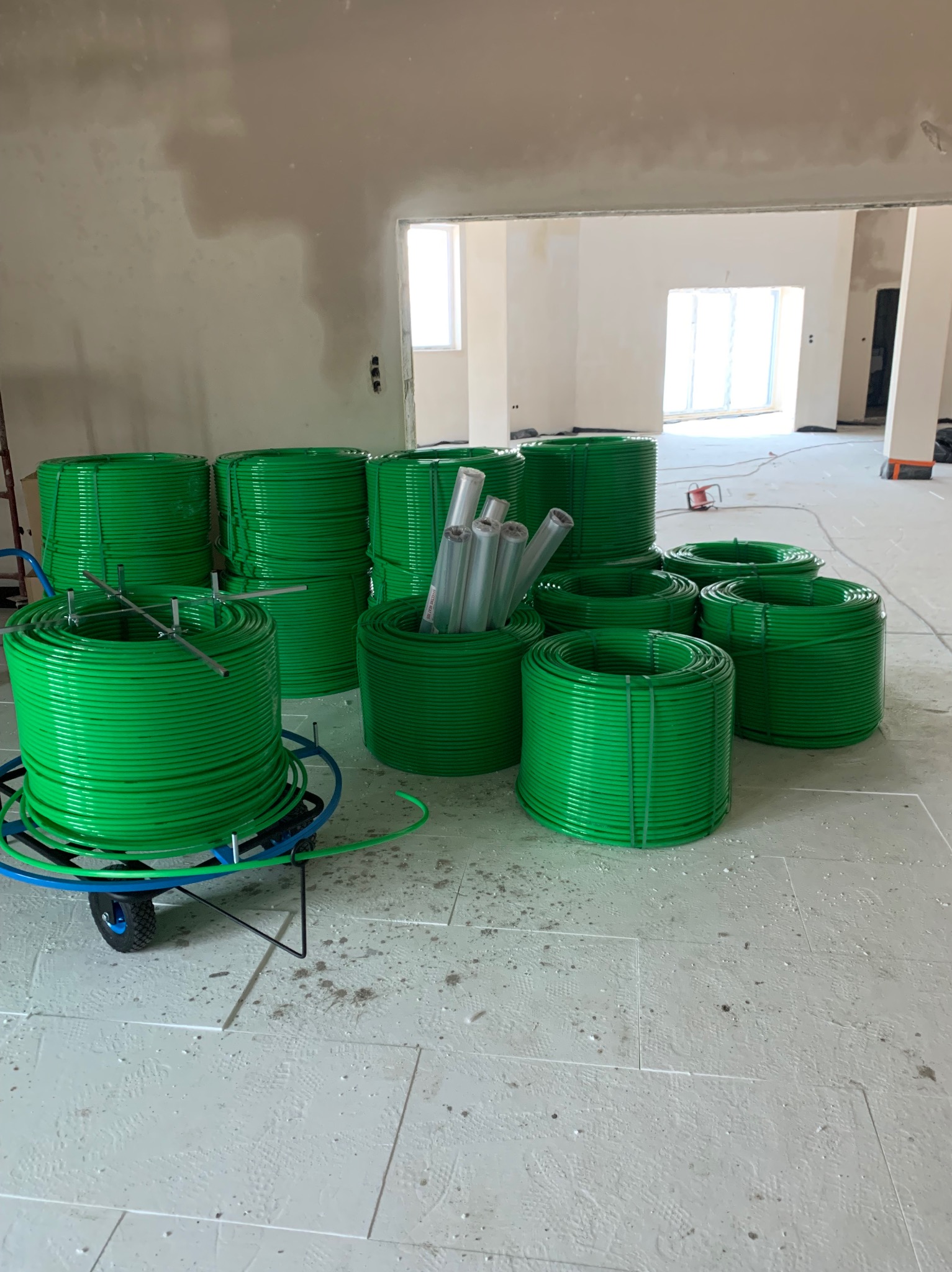 Przygotowane zwoje zielonych rur na białym styropianie podłogowym, gotowe do montażu ogrzewania podłogowego w surowym wnętrzu budynku.