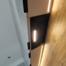 Nowoczesna kuchnia z białymi szafkami, czarnymi uchwytami i drewnianym blatem. Podświetlenie LED podkreśla minimalistyczny design i dodaje elegancji.