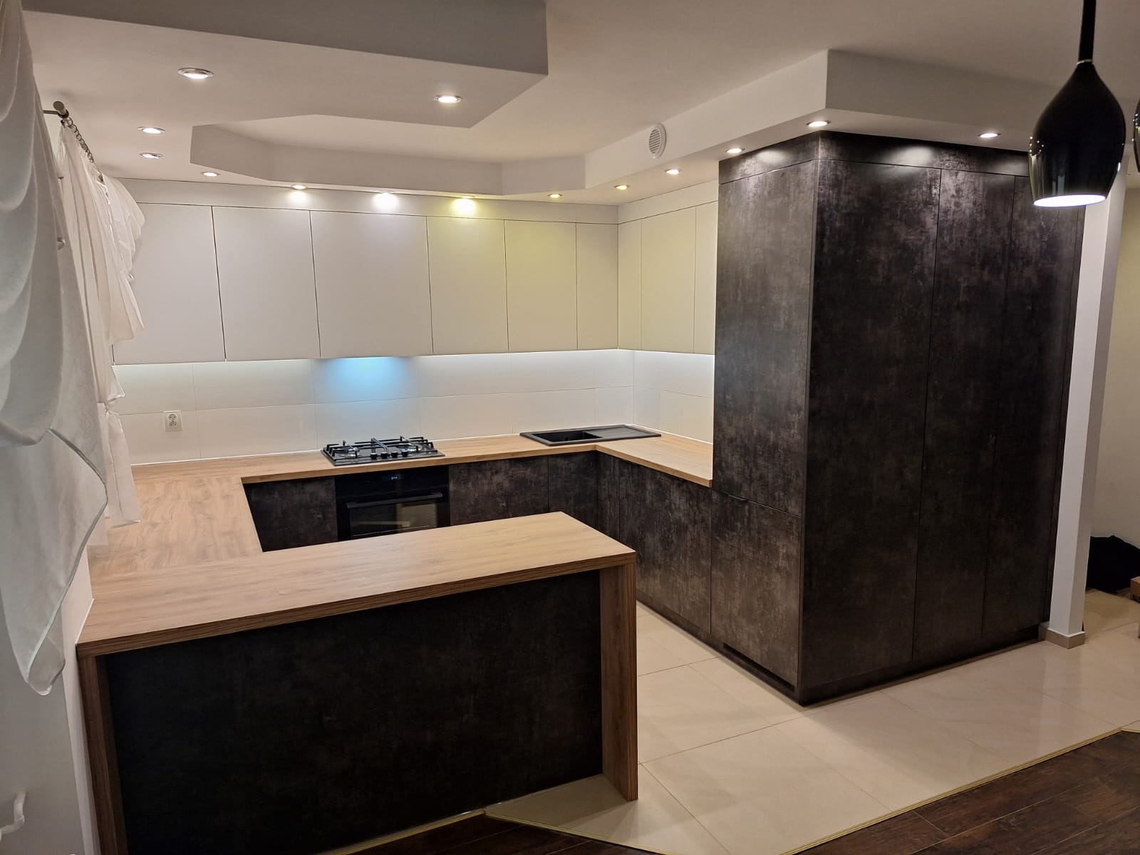 Nowoczesna kuchnia z wyspą: białe szafki górne i ciemne, teksturowane dolne. Blat drewnopodobny, oświetlenie podszafkowe. Minimalistyczny design, widok na płytę grzewczą.