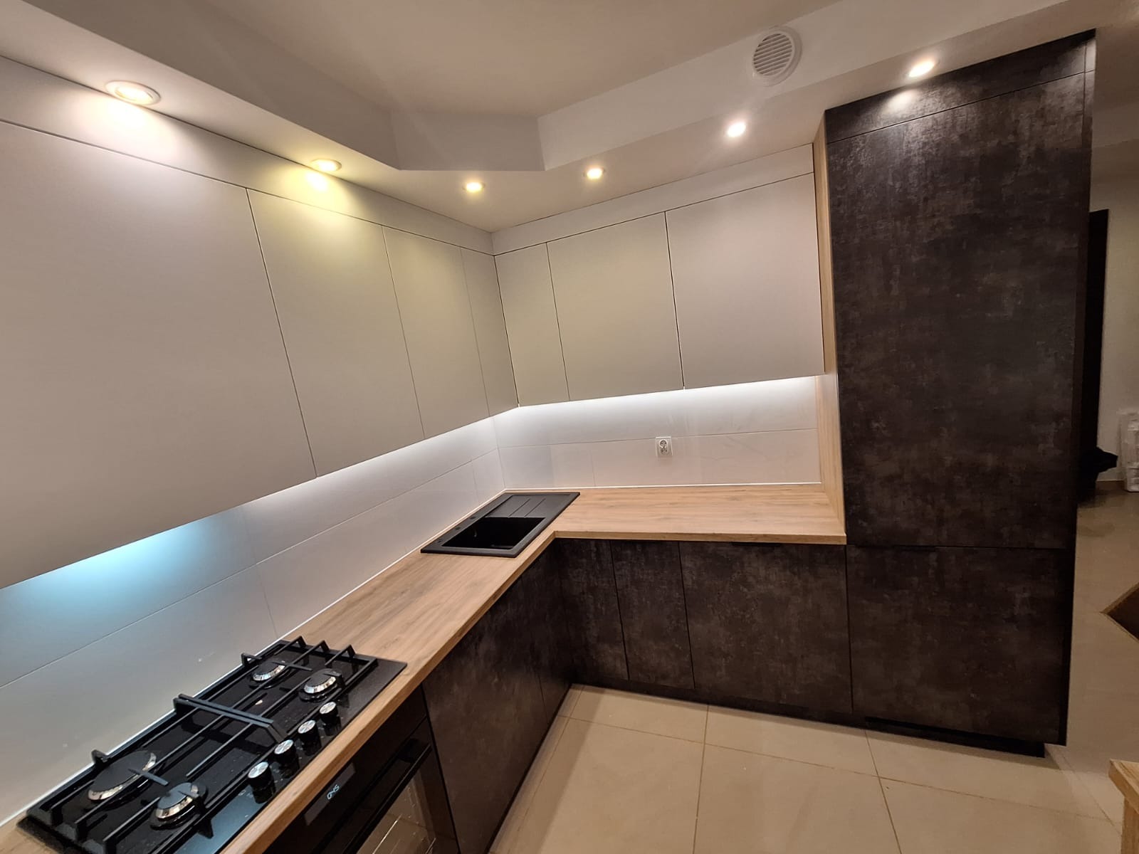 Nowoczesna kuchnia w Starym Gronowie z białymi szafkami górnymi i ciemnymi dolnymi, drewniany blat, oświetlenie LED pod szafkami i punktowe w suficie.