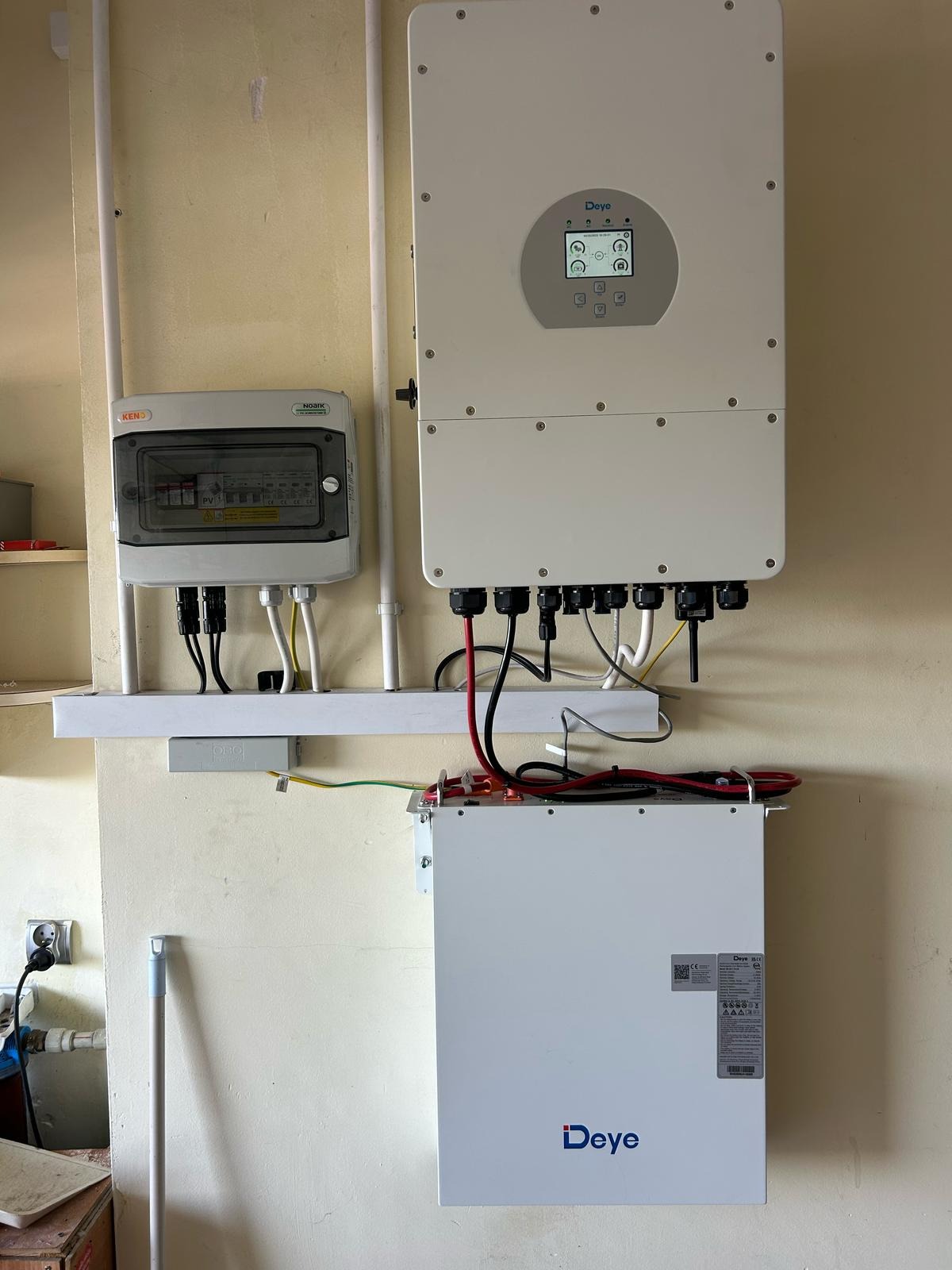 Kompletna instalacja fotowoltaiczna w pomieszczeniu: falownik Deye, rozdzielnica i akumulator. Widoczne przewody i elementy montażowe. Całość zamontowana na ścianie.