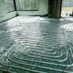 Rozłożona instalacja ogrzewania podłogowego na folii z siatką w surowym wnętrzu. Widoczne rury grzewcze w kształcie meandrów i pętelek przed wylaniem posadzki.