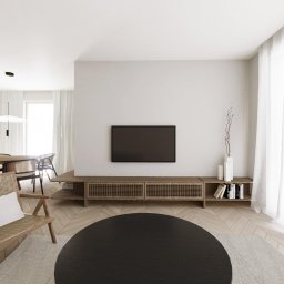 Architektura wnętrz Magdalena Gołdyn Studio Projektowe - Jasne wnętrze w stylu skandynawskim z drewnianą podłogą w jodełkę, telewizorem na ścianie i wiklinowym fotelem z poduszką. Minimalistyczny design.