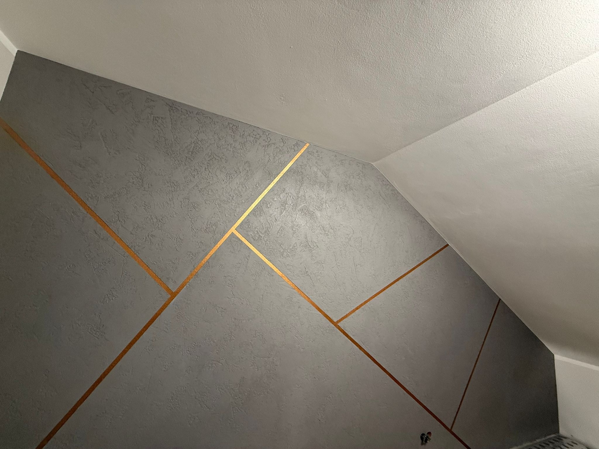 Szara ściana z dekoracyjną fakturą i złotymi liniami w pokoju na poddaszu w Nowym Sączu. Geometryczny wzór, nowoczesny design.