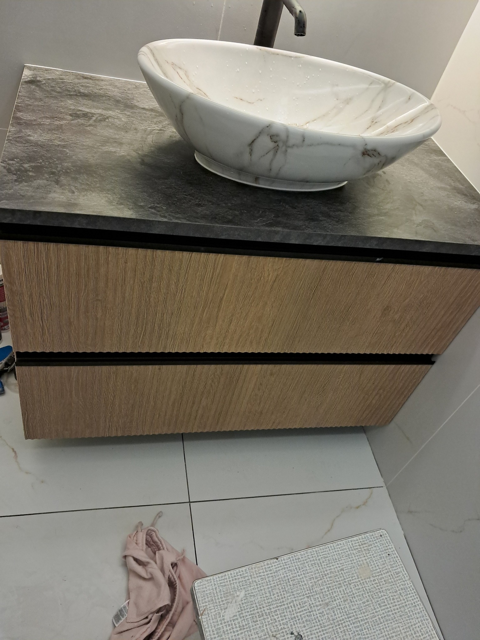 Nowoczesna łazienka: umywalka nablatowa w marmurowym wzorze, szafka z drewnopodobnym frontem i blatem imitującym kamień, czarna bateria.