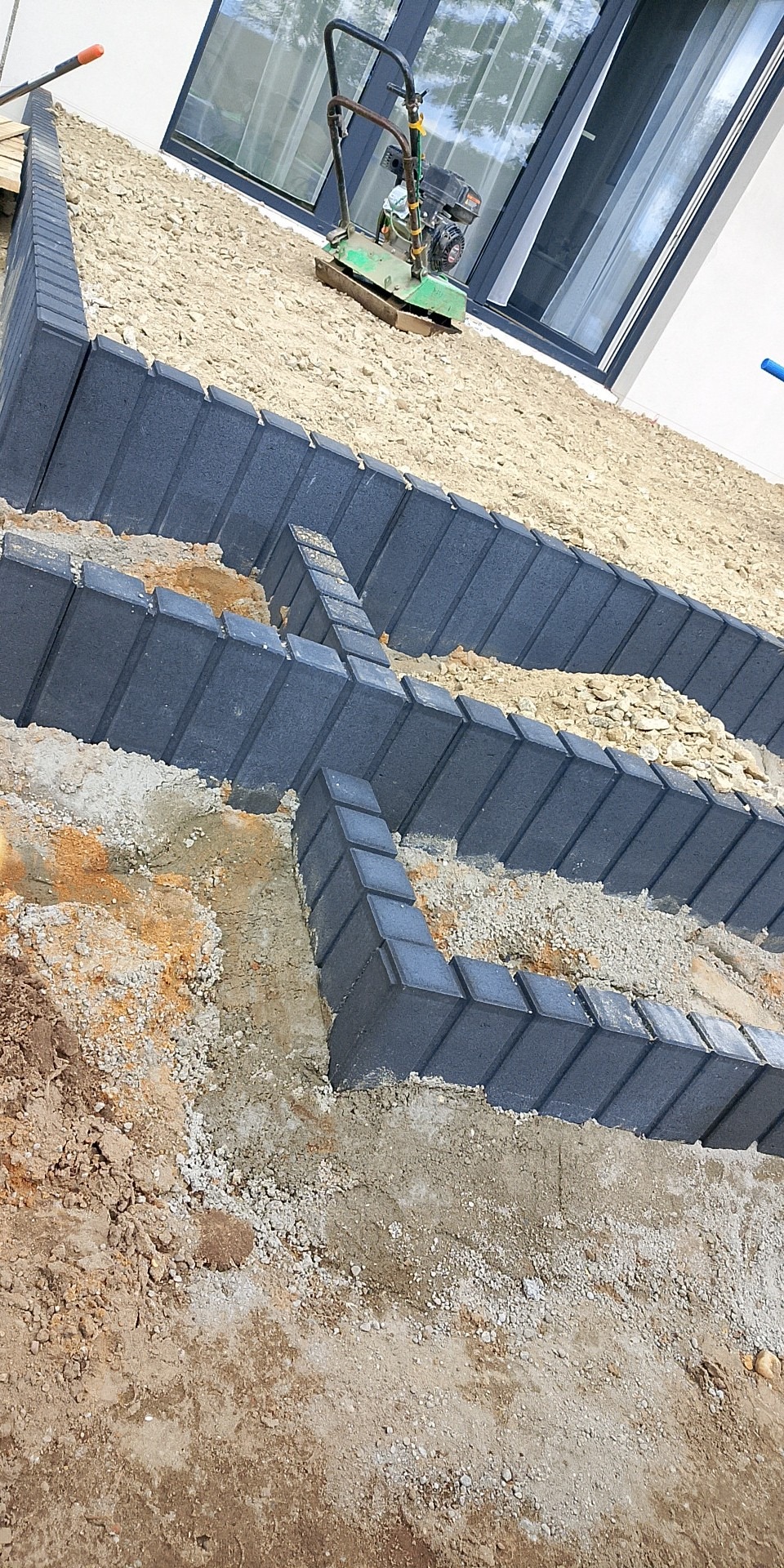 Układanie obrzeży z ciemnej kostki brukowej na podsypce, zagęszczarka obok, widok z góry, etap prac przygotowawczych do ułożenia nawierzchni.