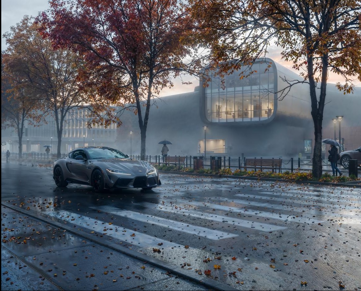 Szary sportowy samochód na mokrej ulicy z jesiennymi liśćmi, na tle nowoczesnego budynku w mglisty dzień. Unikalny kadr z niskiej perspektywy.