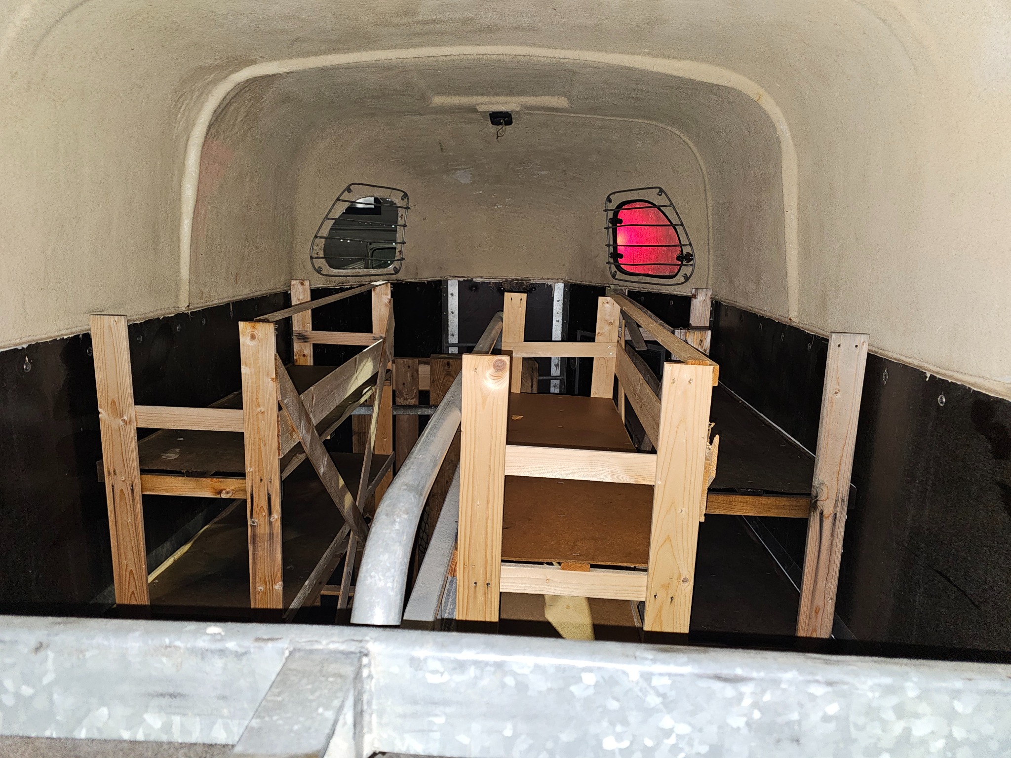 Wnętrze furgonetki w trakcie adaptacji: drewniana konstrukcja pod podłogę i ściany, widoczne okna z kratami. Prace wykończeniowe w pojeździe.