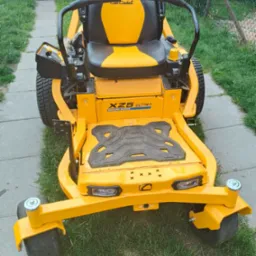 Żółta kosiarka samojezdna Cub Cadet XZ5 Ultima na trawniku, widziana z przodu. Widoczny fragment chodnika i ogrodzenia. Sprzęt gotowy do pracy.