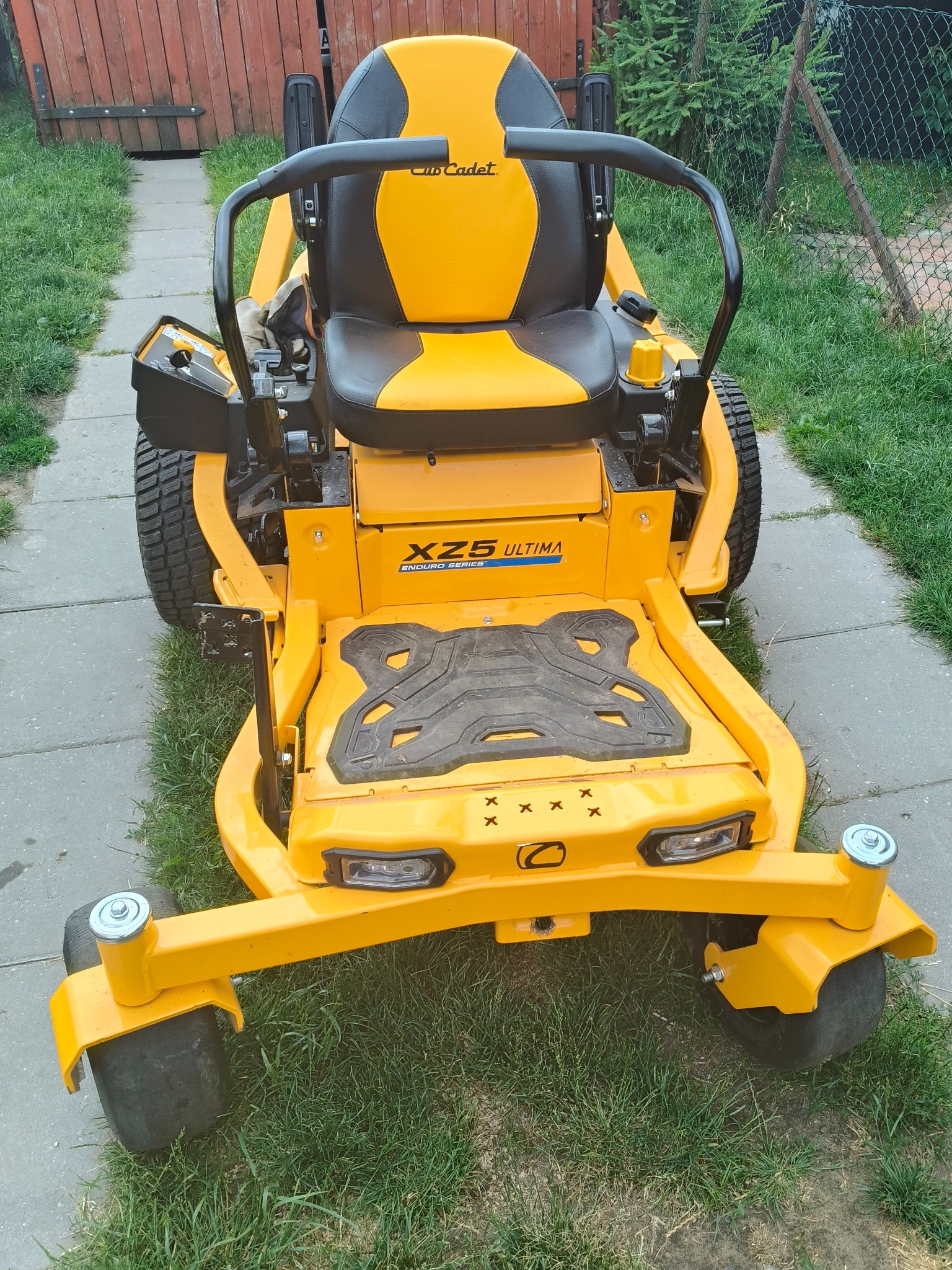 Żółta kosiarka samojezdna Cub Cadet XZ5 Ultima na trawniku, widziana z przodu. Widoczny fragment chodnika i ogrodzenia. Sprzęt gotowy do pracy.