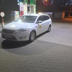 Atom Tomasz Kania - Białe kombi taxi Ford Mondeo na stacji benzynowej BP, Wrocław 4393. Widoczny dystrybutor autogazu i Paczkomat. Nocne ujęcie z niskim oświetleniem.