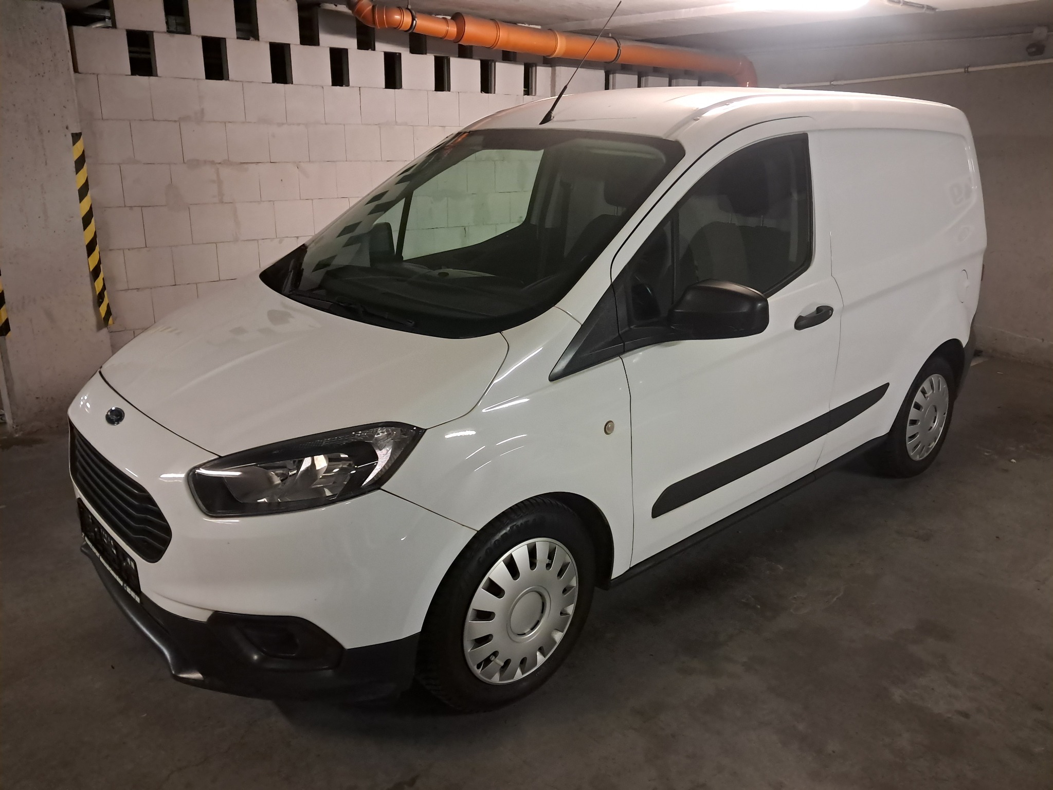 Biały, dostawczy Ford Transit Courier zaparkowany w garażu, widok z przodu pod kątem. Auto czyste, gotowe do transportu.