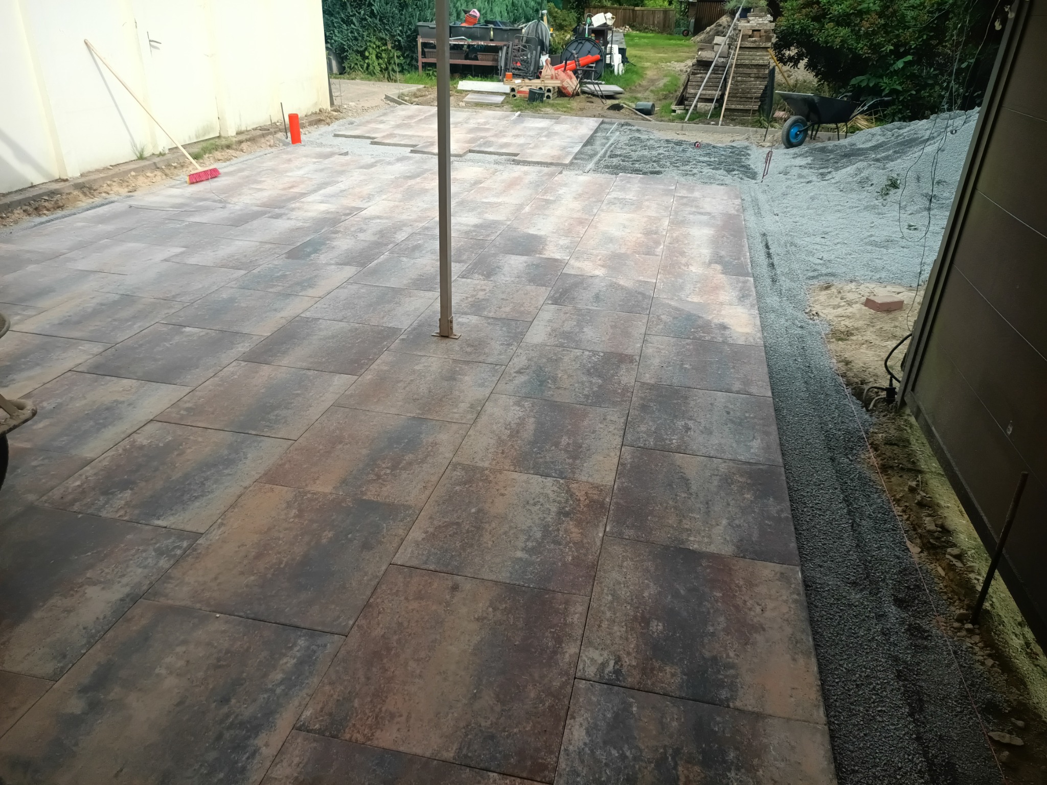 Częściowo ułożona kostka brukowa na posesji. Widoczny fragment podwórka z przygotowanym podłożem i narzędziami. Kostka w odcieniach brązu i szarości.