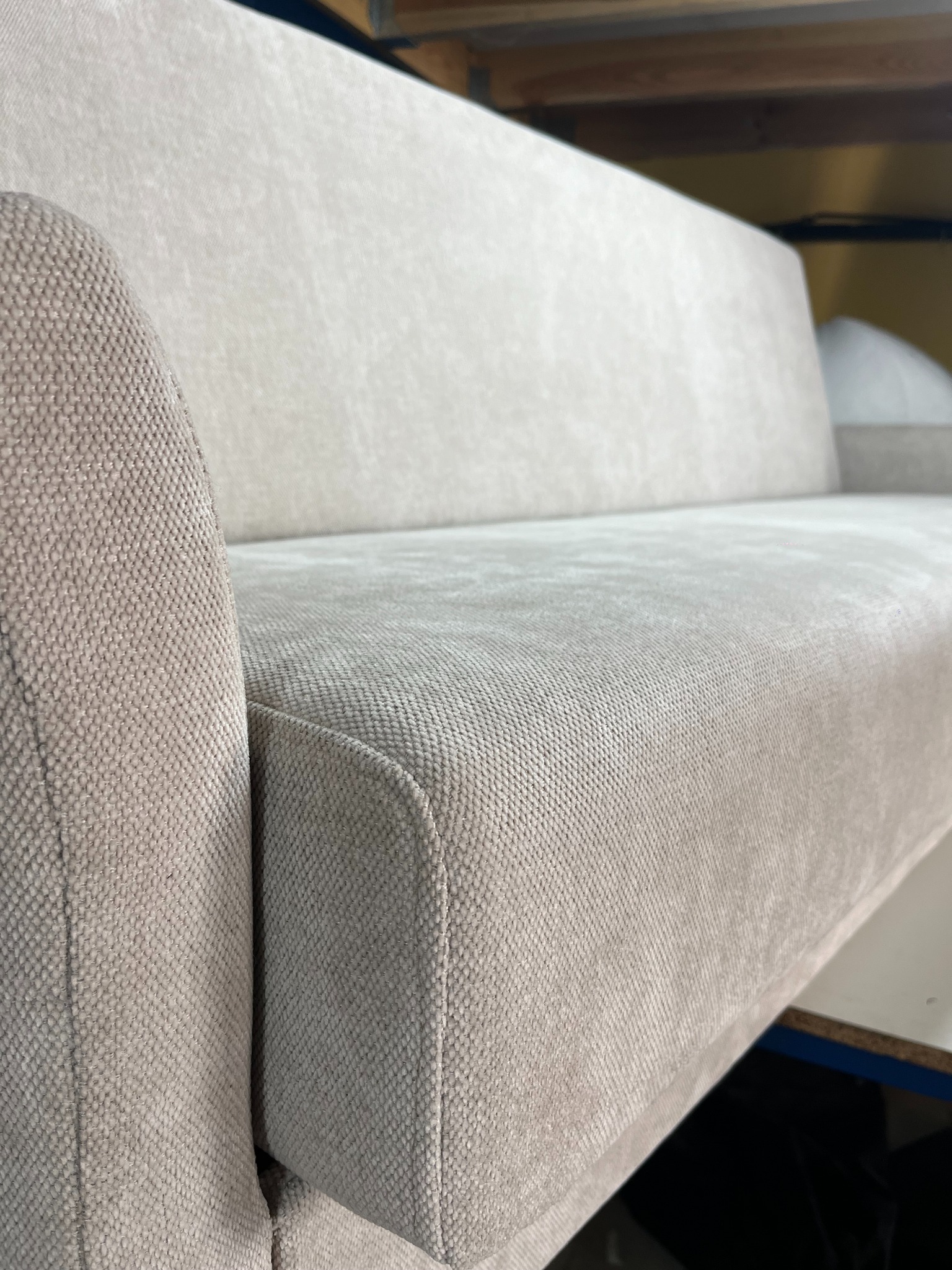 Beżowa sofa tapicerowana, zbliżenie na bok i siedzisko. Widoczna faktura materiału i staranne wykończenie krawędzi. Ustawiona w warsztacie.